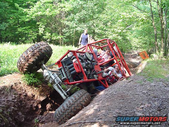 Red off-road buggy with people inside stuck in a deep ditch on a dirt trail