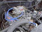 Engine bay with carburetor and blue spark plug wires. Some dirt and grime visible