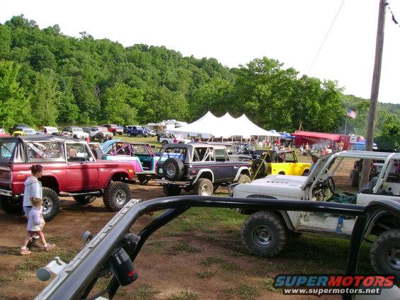 Red 1966 Ford Bronco with black top and roll cage, parked on dirt lot