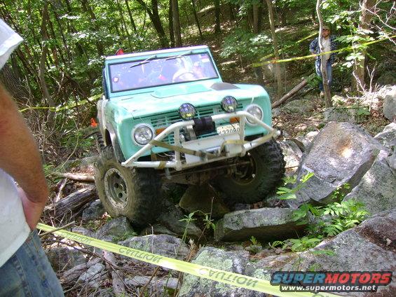Teal 1969 Ford Bronco off-roading over rocks with a winch