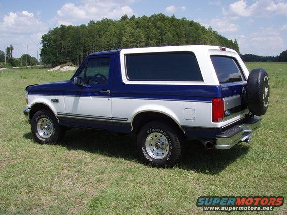 Blue and white 1996 Ford Bronco parked on grass with trees in background