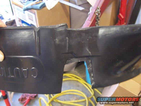 Black plastic automotive part with embossed "CAUTION" text, showing damage and cut edges