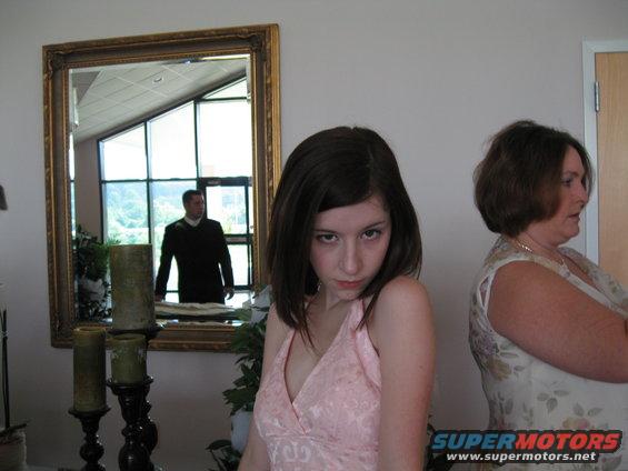 Interior scene with a young woman in a pink dress and an older woman, with a man reflected in a mirror