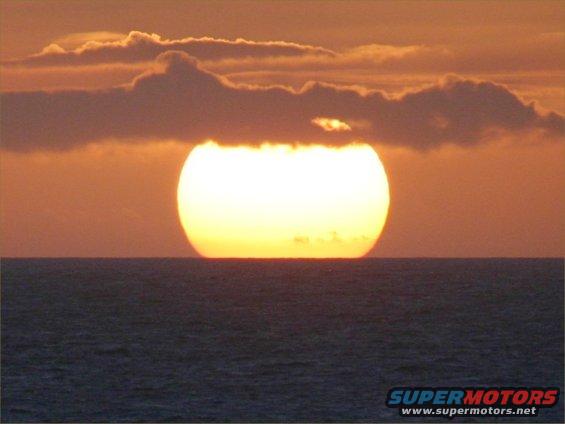 Sunset over dark ocean with clouds, Supermotors.net logo visible