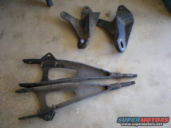 Two suspension control arms and two mounting brackets on a concrete floor