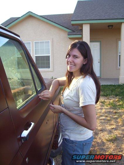 Brown SUV side view, woman leaning on door, house in background