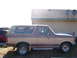 1990 Ford Bronco - A two-tone brown Ford Bronco is parked outside a building with satellite dishes on the roof.