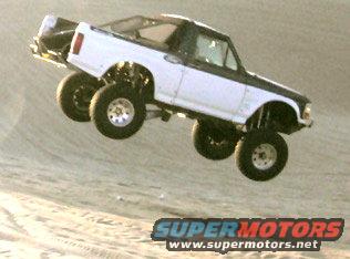 White and black lifted truck airborne over sand dunes