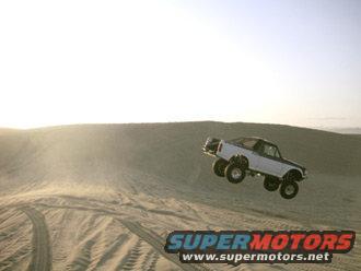 White 1996 Ford Bronco mid-air jump over sand dune, lifted suspension, off-road tires