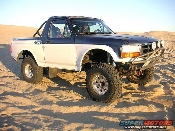 Two-tone 1996 Ford Bronco prerunner with off-road modifications parked in sand dunes
