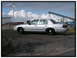 1998 Ford Crown Victoria - Side view of a silver 1998 Ford Crown Victoria parked outdoors near industrial structures.