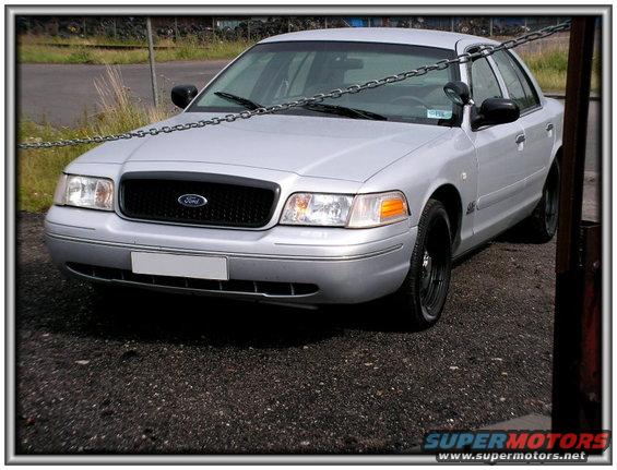 Silver Ford Crown Victoria with black grille and black wheels. Chain across the front