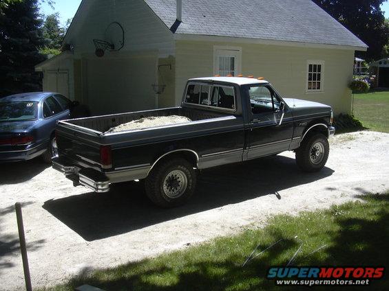 Dark blue and gray Ford F-250 pickup truck parked in a driveway with sand in the bed. A blue sedan is parked to its left