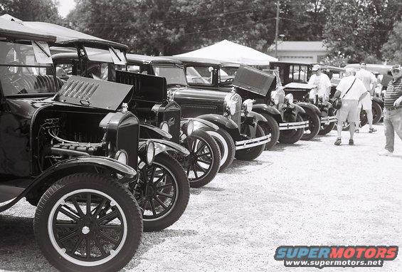 Several black Ford Model T cars parked in a row, hoods open, at an outdoor event