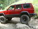 1996 Jeep Cherokee - A red Jeep Cherokee navigates a rocky trail with a person observing from a nearby rock.
