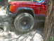 1996 Jeep Cherokee - A red Jeep Cherokee is shown off-roading on a rocky trail, with its front tire angled over a boulder.