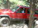 1996 Jeep Cherokee - A red 1996 Jeep Cherokee navigates a rocky, wooded trail, with dust billowing from its tires.
