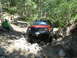 1996 Jeep Cherokee - A red Jeep Cherokee tackles a challenging, rocky off-road path in a wooded area.