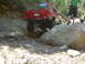 1996 Jeep Cherokee - A red 1996 Jeep Cherokee tackles a challenging off-road obstacle on a muddy and rocky trail, with another vehicle visible in the background.