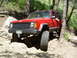 1996 Jeep Cherokee - A red 1996 Jeep Cherokee is shown off-roading on a rocky trail, with a person visible in the driver's seat.