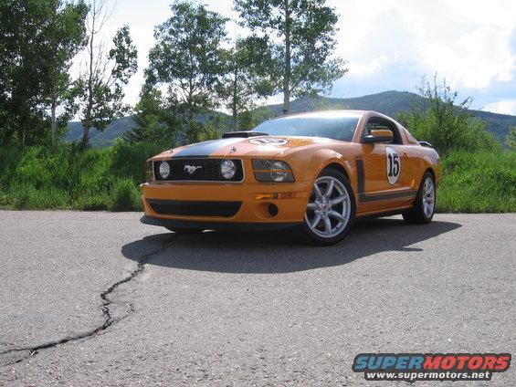 Orange Ford Mustang with black racing stripes and number 15 on the side, parked on cracked asphalt