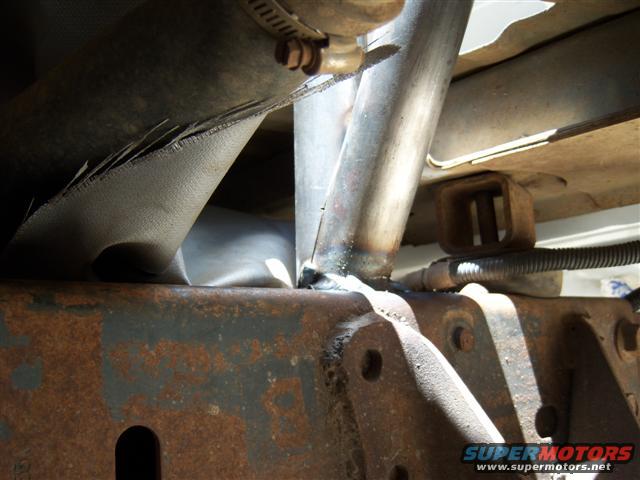 Close-up of rusty vehicle frame with exhaust pipe and metal bracing, showing welds and a hose clamp