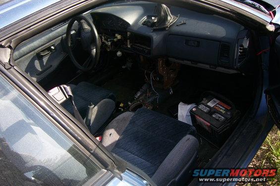 1993 Mazda MX-6 interior with dark blue seats, disassembled dashboard, and battery on the floor
