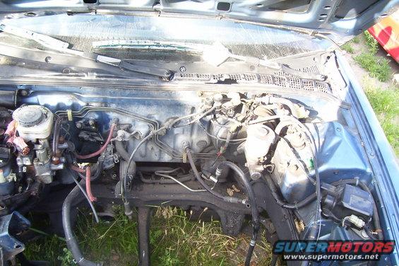 Engine bay of a blue car with hoses and wires visible