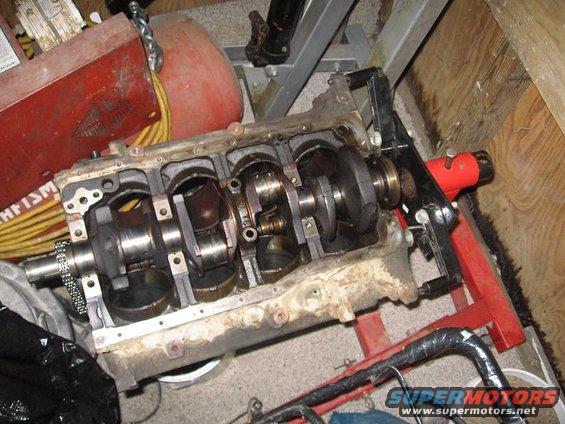 Engine block with crankshaft and connecting rods visible, mounted on a red engine stand