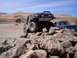 1989 Ford Bronco - A modified green SUV navigates a rocky obstacle course with a blue pickup truck in the background.