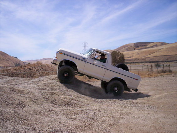 White Ford Bronco climbing a gravel hill, lifted suspension, spare tire mounted on rear