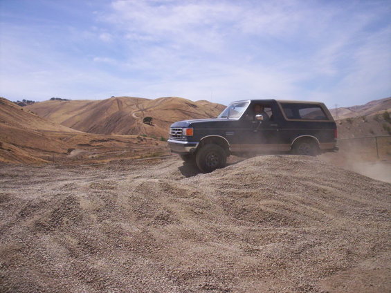 Dark blue 1989 Ford Bronco with tan top driving on a gravel hill
