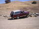 1989 Ford Bronco - A maroon 1989 Ford Bronco is parked on a dirt road with a spare tire mounted on the rear.