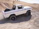 1989 Ford Bronco - White Ford Bronco navigating rough terrain on a sunny day.