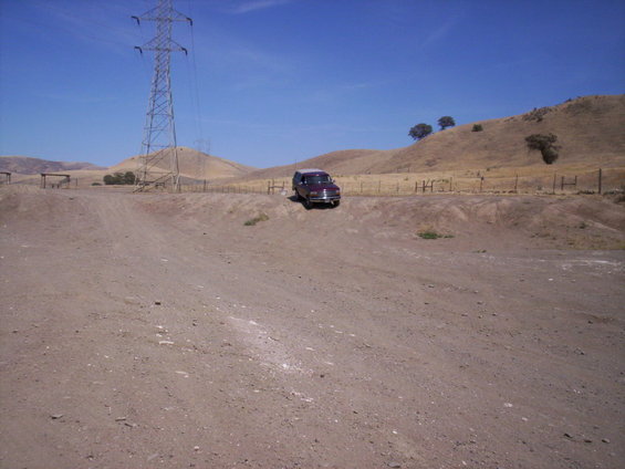 Maroon Ford Bronco parked on a dirt road with hills and a power tower in the background