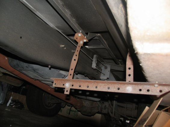 Rusty metal running board mounting brackets attached to the undercarriage of a vehicle
