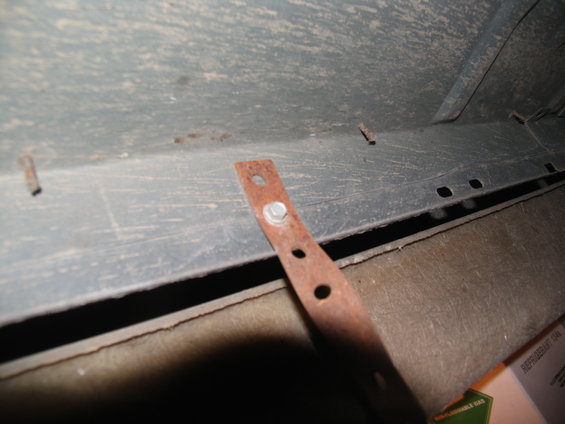 Close-up of a rusty metal bracket bolted to the underside of a vehicle, showing mounting holes