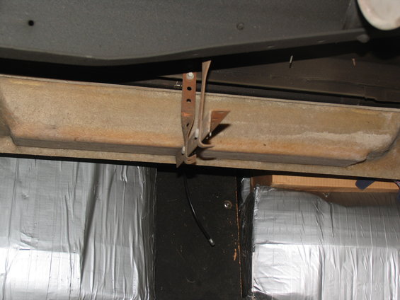 Rusty metal bracket attached to a vehicle's undercarriage, with silver insulation visible below