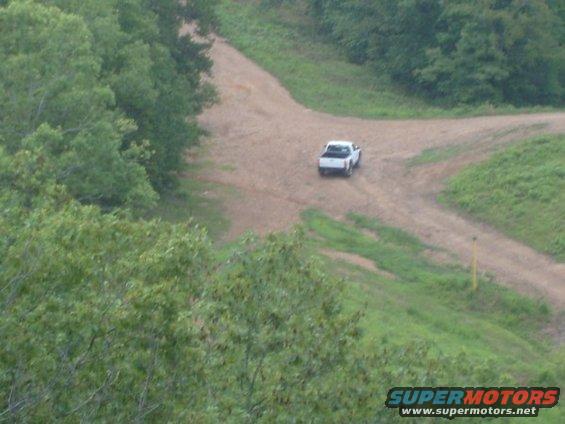 White pickup truck on a dirt road, viewed from above and behind