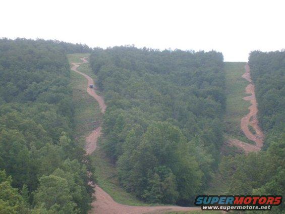 SUV on a dirt road climbing a hill through a forest