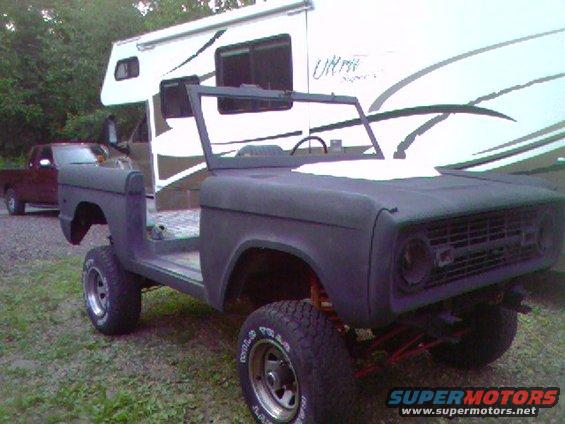 Unfinished Ford Bronco body, dark primer, with RV in background and red truck to the left