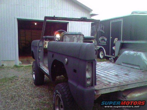 Dark gray Ford Bronco with no top or doors, sitting on a gravel driveway in front of a garage