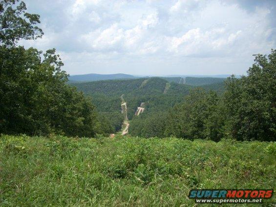 Mountain landscape with cleared ski slopes and trees under a cloudy sky. Watermark reads SUPERMOTORS