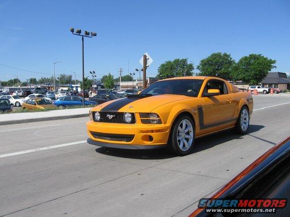 Orange 2007 Saleen S-302 Mustang with black stripe on hood, driving on a road