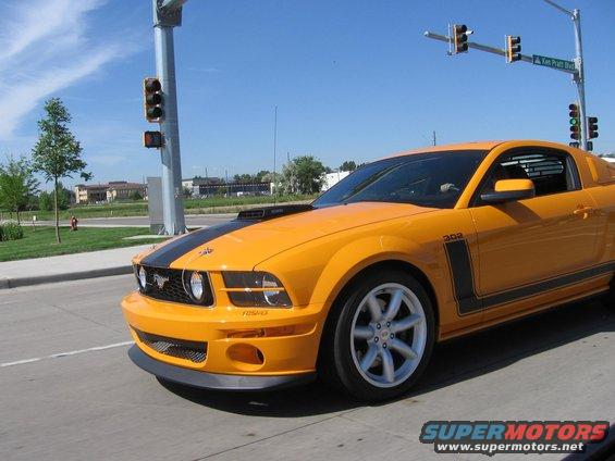 Yellow Ford Mustang with black stripes, driving on a sunny day