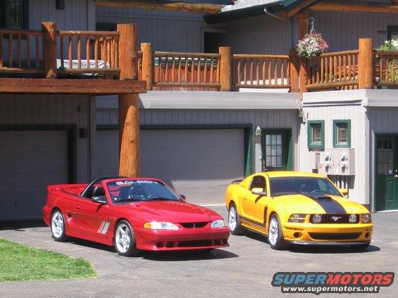 Red convertible Mustang and yellow coupe Mustang parked in front of a house