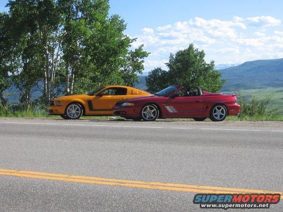 Red convertible Mustang and yellow coupe Mustang parked on a roadside