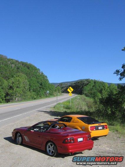 Red convertible Mustang and orange coupe Mustang parked roadside