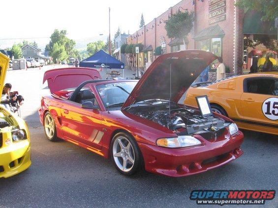 Red convertible with hood open, showing engine. Yellow car with racing stripe and number 15 visible