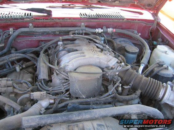 Red engine bay with Nissan branding on the intake manifold. Dusty and cluttered with hoses and wires